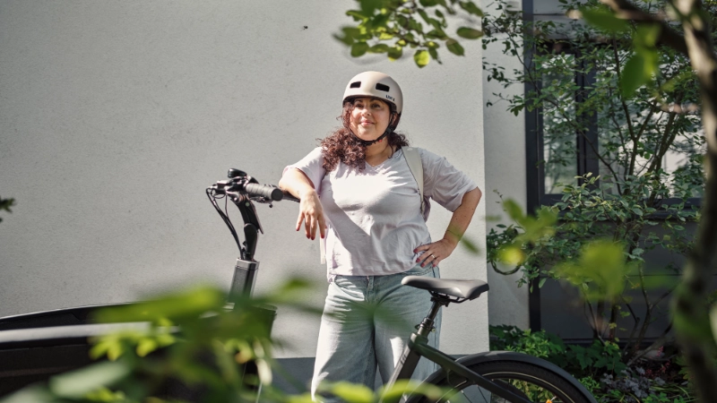 Frau mit Locken lehnt am JobRad, im Vordergrund Pflanzen Frau mit Locken lehnt am JobRad, im Vordergrund Pflanzen