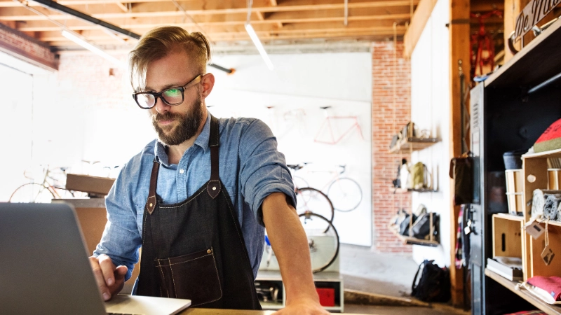 Fachhändler im Fahrradgeschäft steht am Tresen und schaut komnzentriert in den Laptop. Er nutzt die Partner API Fachhändler im Fahrradgeschäft steht am Tresen und schaut komnzentriert in den Laptop. Er nutzt die Partner API