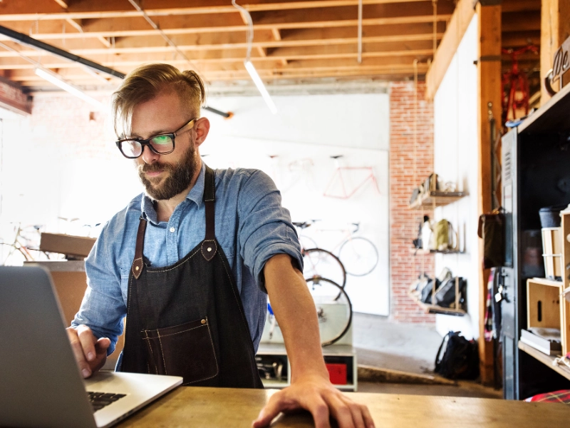 Fachhändler im Fahrradgeschäft steht am Tresen und schaut komnzentriert in den Laptop. Er nutzt die Partner API Fachhändler im Fahrradgeschäft steht am Tresen und schaut komnzentriert in den Laptop. Er nutzt die Partner API
