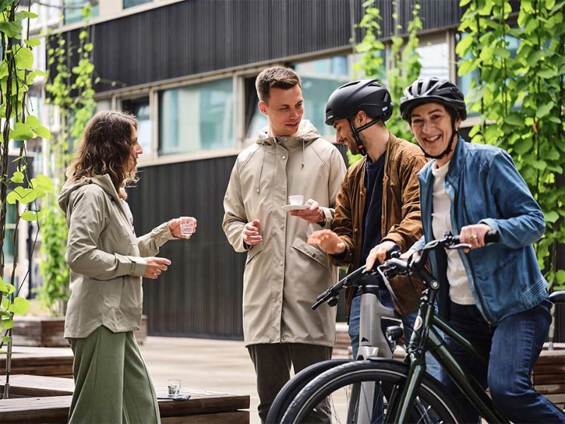 Ein JobRad Team aus vier Personen trinkt Kaffee auf dem JobRad-Campus, eine Frau aus dem Team sitzt auf dem Fahrrad