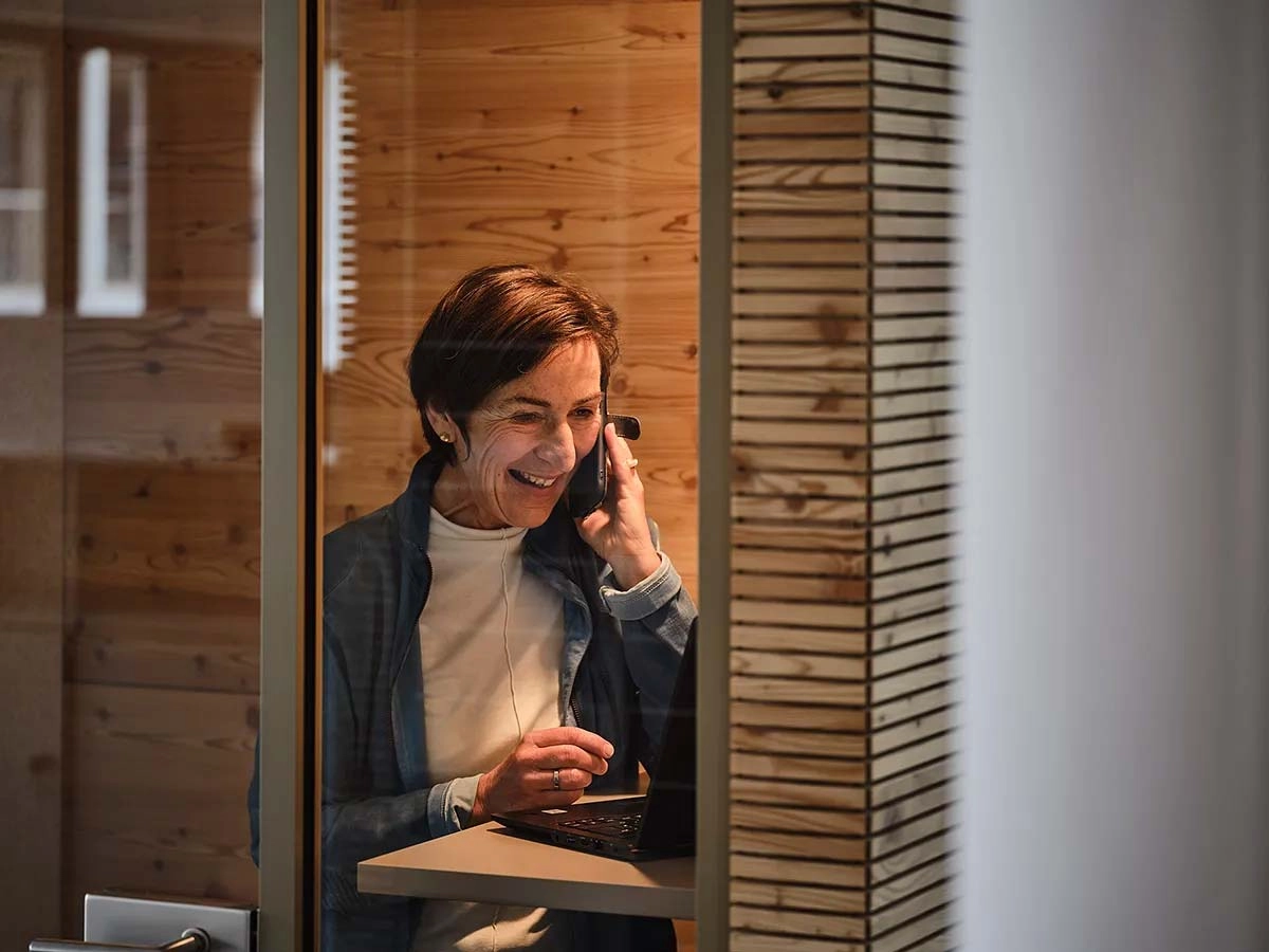 Eine lächelnde ältere Frau sitzt im Büro und telefoniert