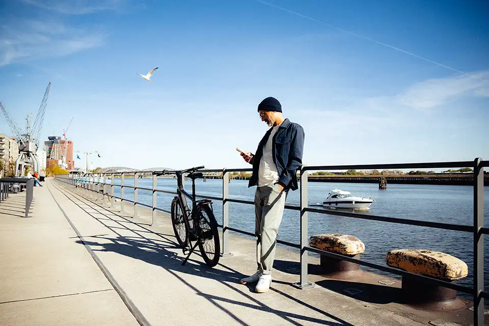 Mann steht mit Dienstrad am Hafen-Kanal und schaut aufs Handy
